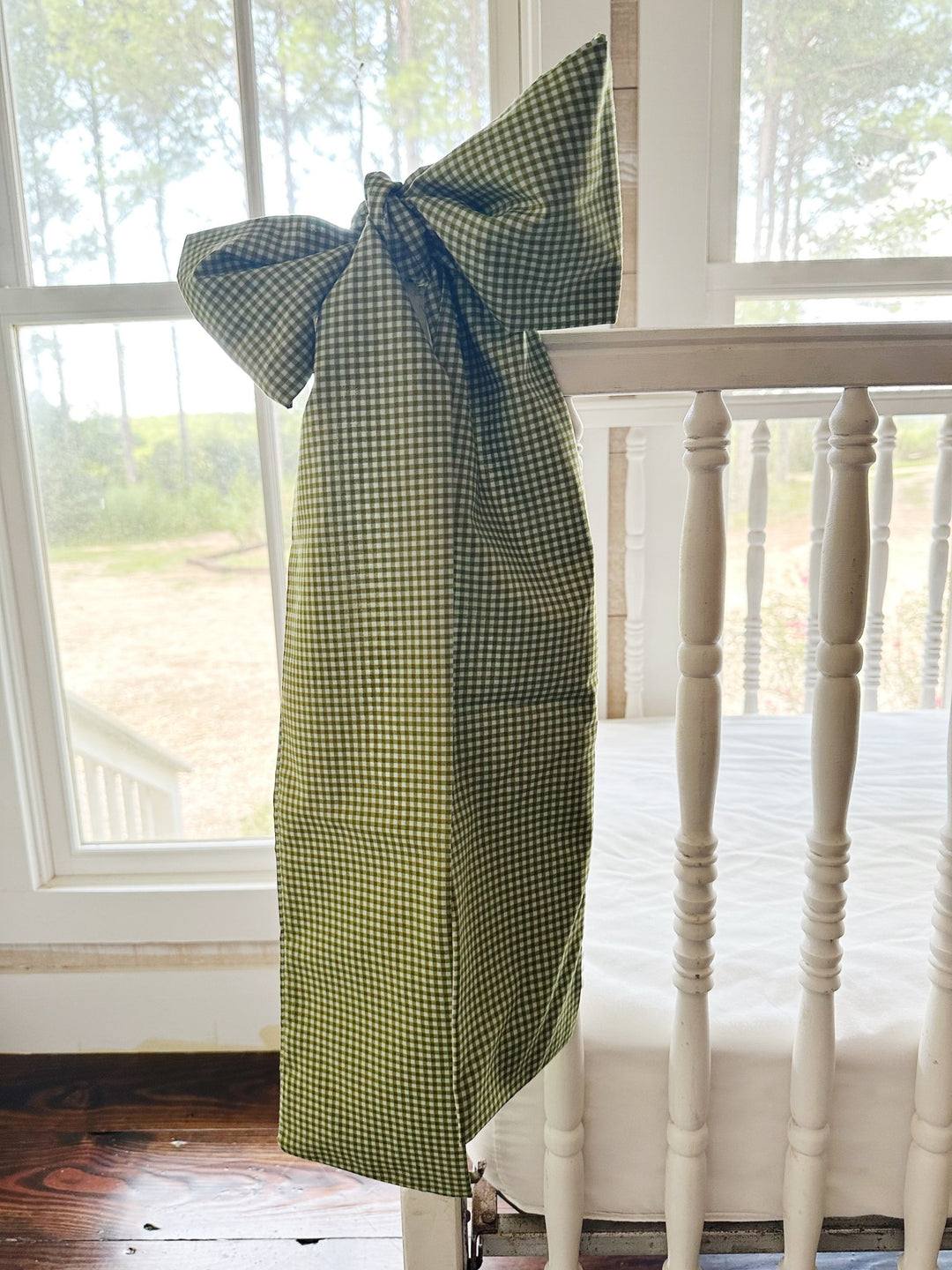 Pine green gingham crib bow tied on a white spindle crib rail in a farmhouse nursery