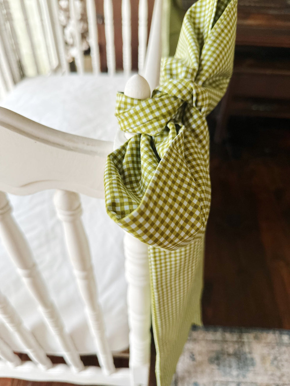 Overhead view of a pine green gingham bow knotted around a white crib corner post