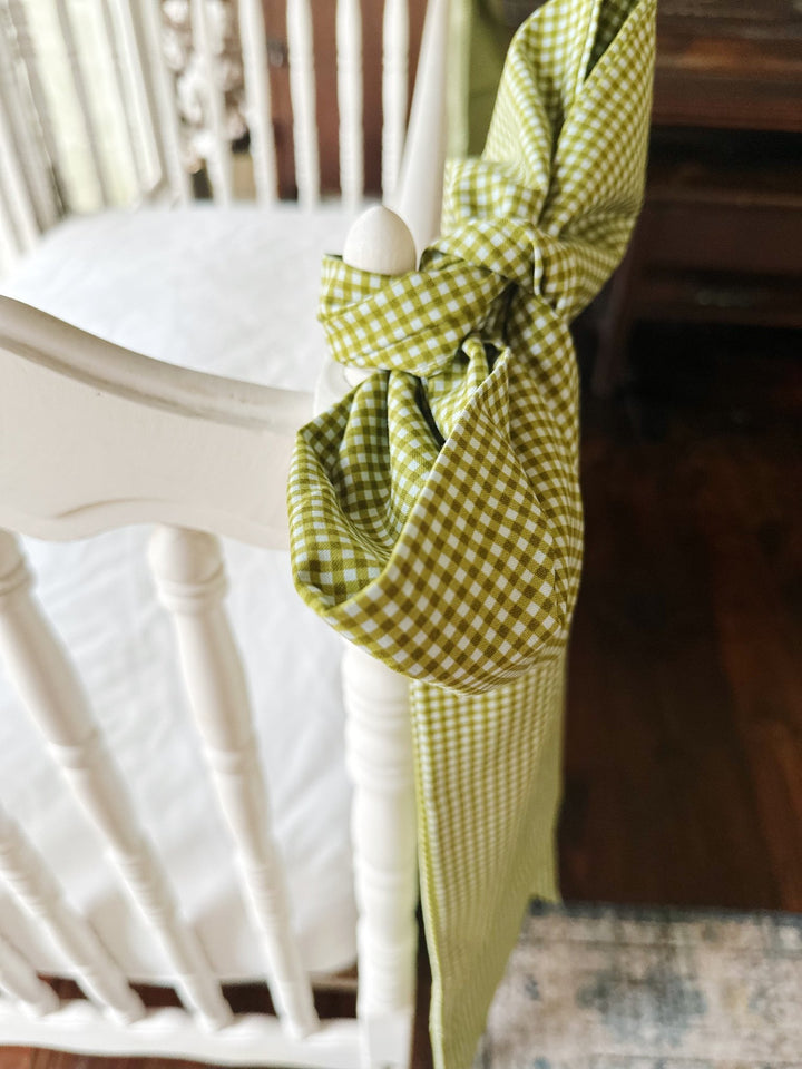 Overhead view of a pine green gingham bow knotted around a white crib corner post