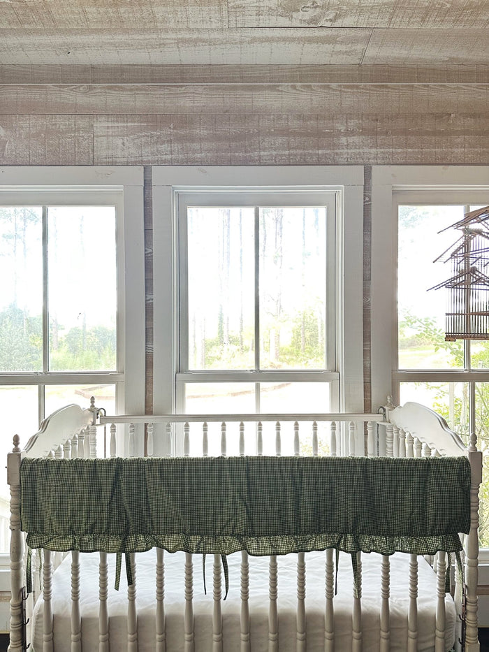 Pine green gingham ruffled crib rail cover on the front rail of a white spindle crib