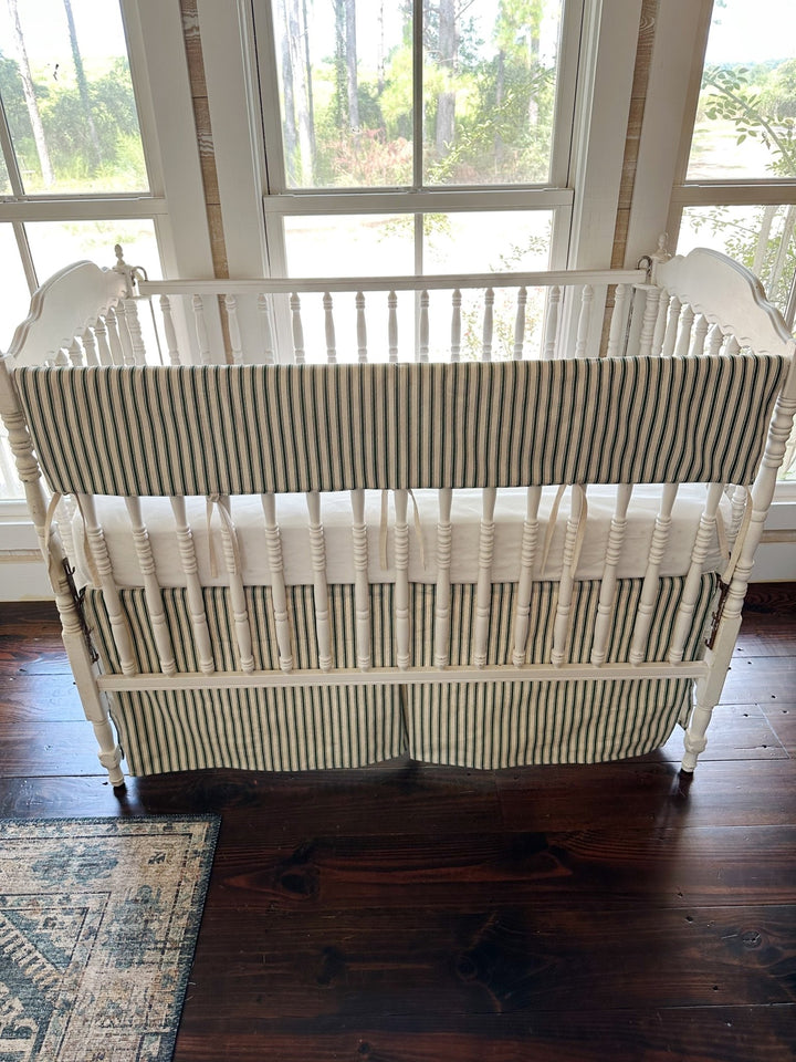 Looking down on the whole crib, the ticking rail cover and skirt against dark pine floors