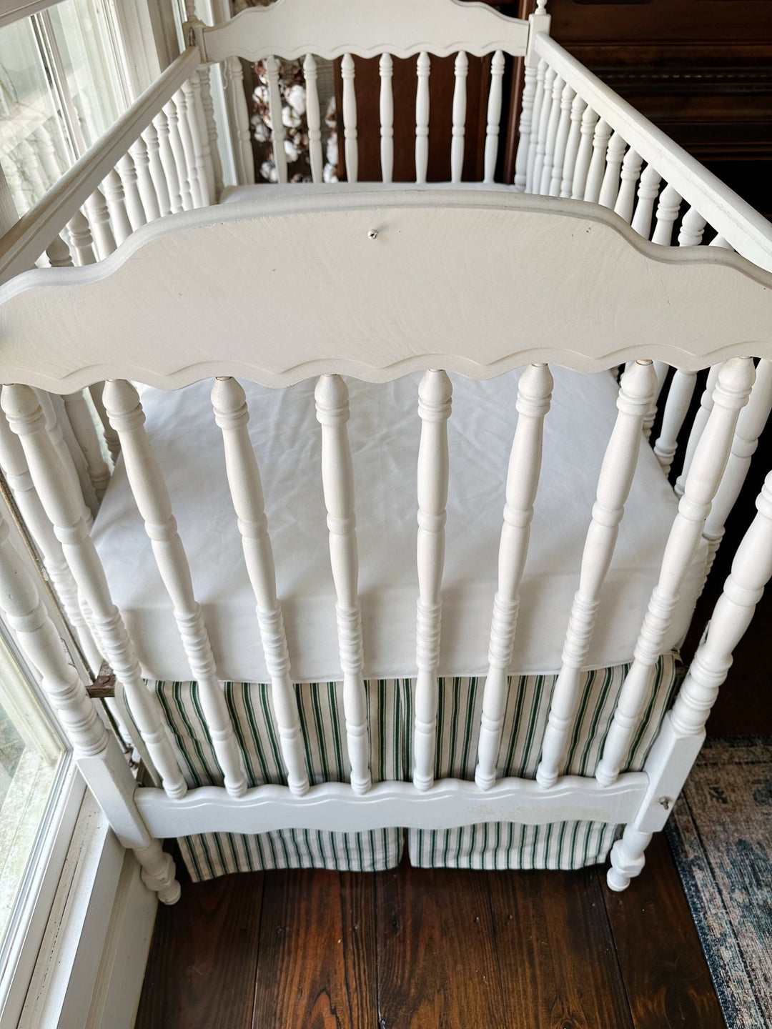 Seen from the end of the crib, the pleated ticking skirt beneath a plain white sheet