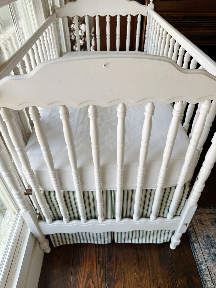Seen from the end of the crib, the pleated ticking skirt beneath a plain white sheet