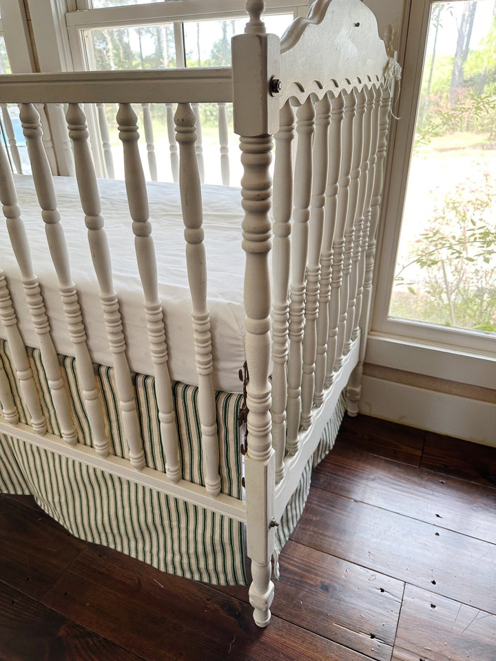 The corner of the crib where the ticking skirt wraps the leg, stripes running to the hem