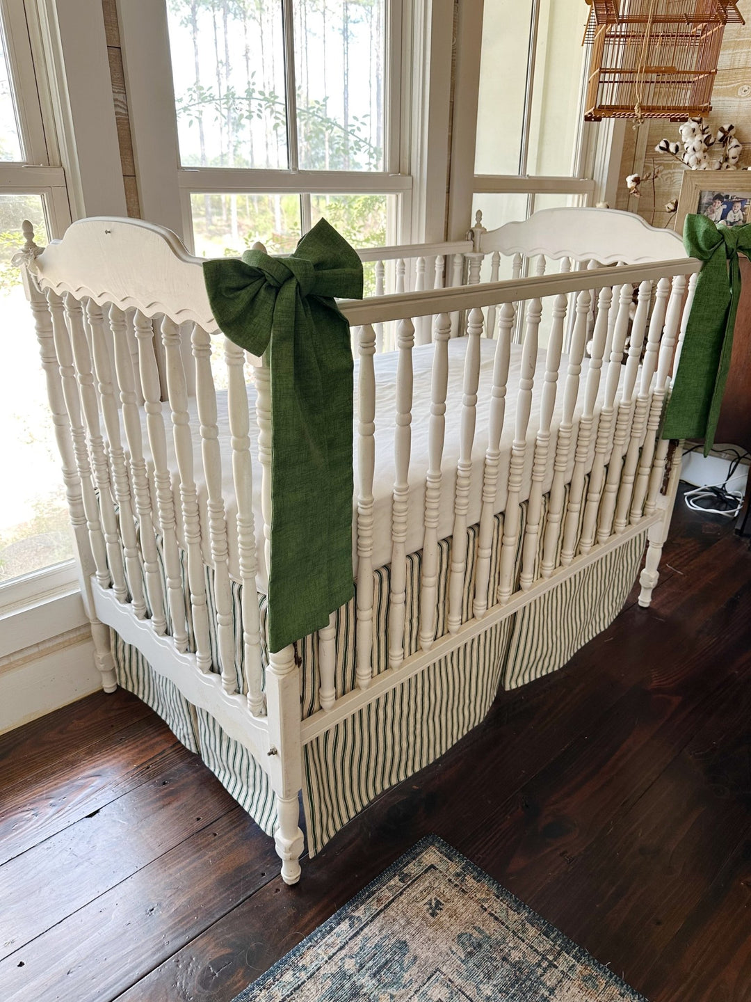 Pine green ticking tailored crib skirt with two solid cypress green sashes tied to the crib posts