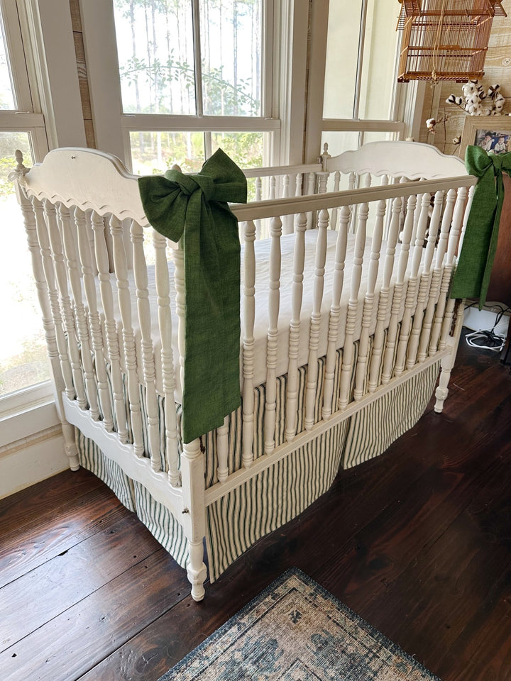 Pine green ticking tailored crib skirt with two solid cypress green sashes tied to the crib posts