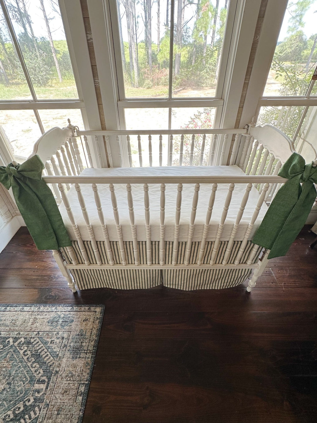 Looking slightly down at the crib, both sashes hanging long against the ticking skirt