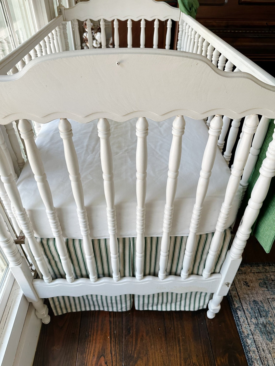 Seen from the end of the crib, the pleated ticking skirt beneath a plain white sheet