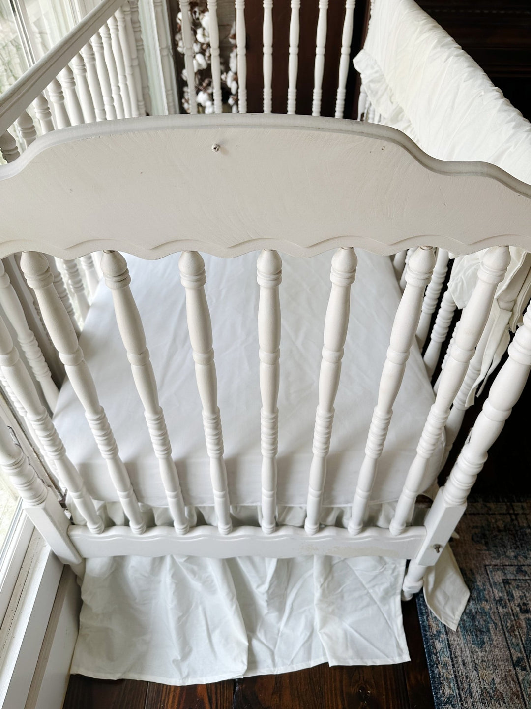 Porcelain crib skirt gathering behind the turned spindles below the mattress line