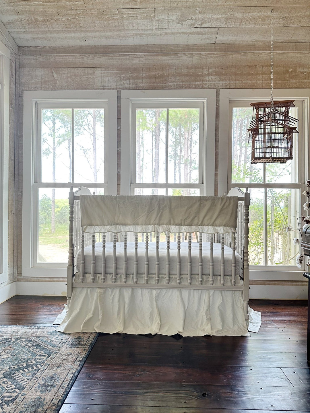 Porcelain crib bedding set styled beneath three windows in a pine-panelled nursery