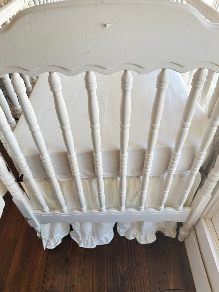 Looking down over the scalloped footboard at the white mattress and the porcelain ruffled skirt beneath