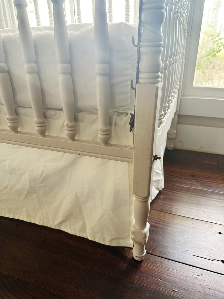 Split corner of the porcelain crib skirt wrapping cleanly around a turned crib leg - High Cotton Textile