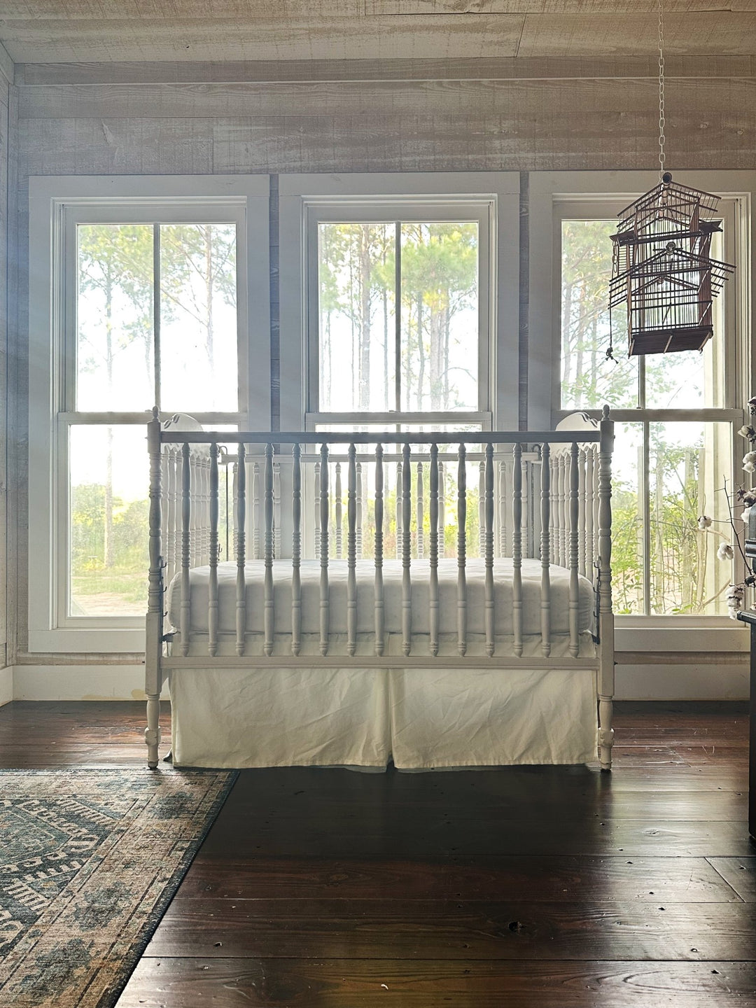 Farmhouse nursery with shiplap walls, dark pine floors and a spindle crib dressed in a porcelain tailored crib skirt - High Cotton Textile