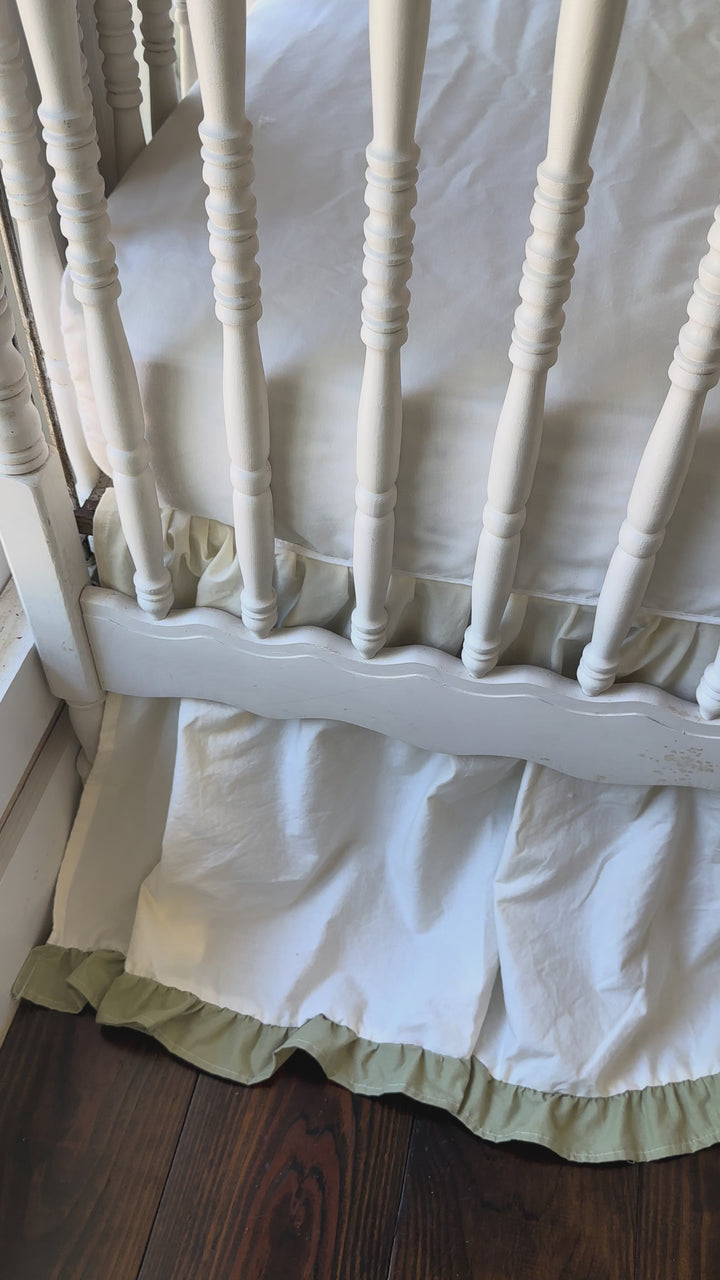 Video of an ivory and sage green ruffled crib skirt and large ivory crib bow set showing the gathered 22 inch drop