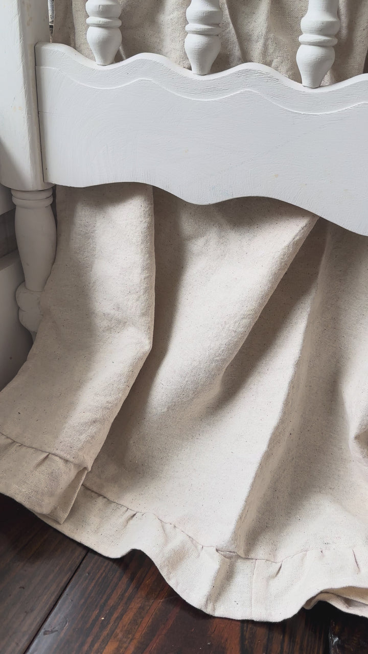 Video of a neutral ruffled crib skirt in natural osnaburg with two large oatmeal crib bows in a nursery - High Cotton Textile