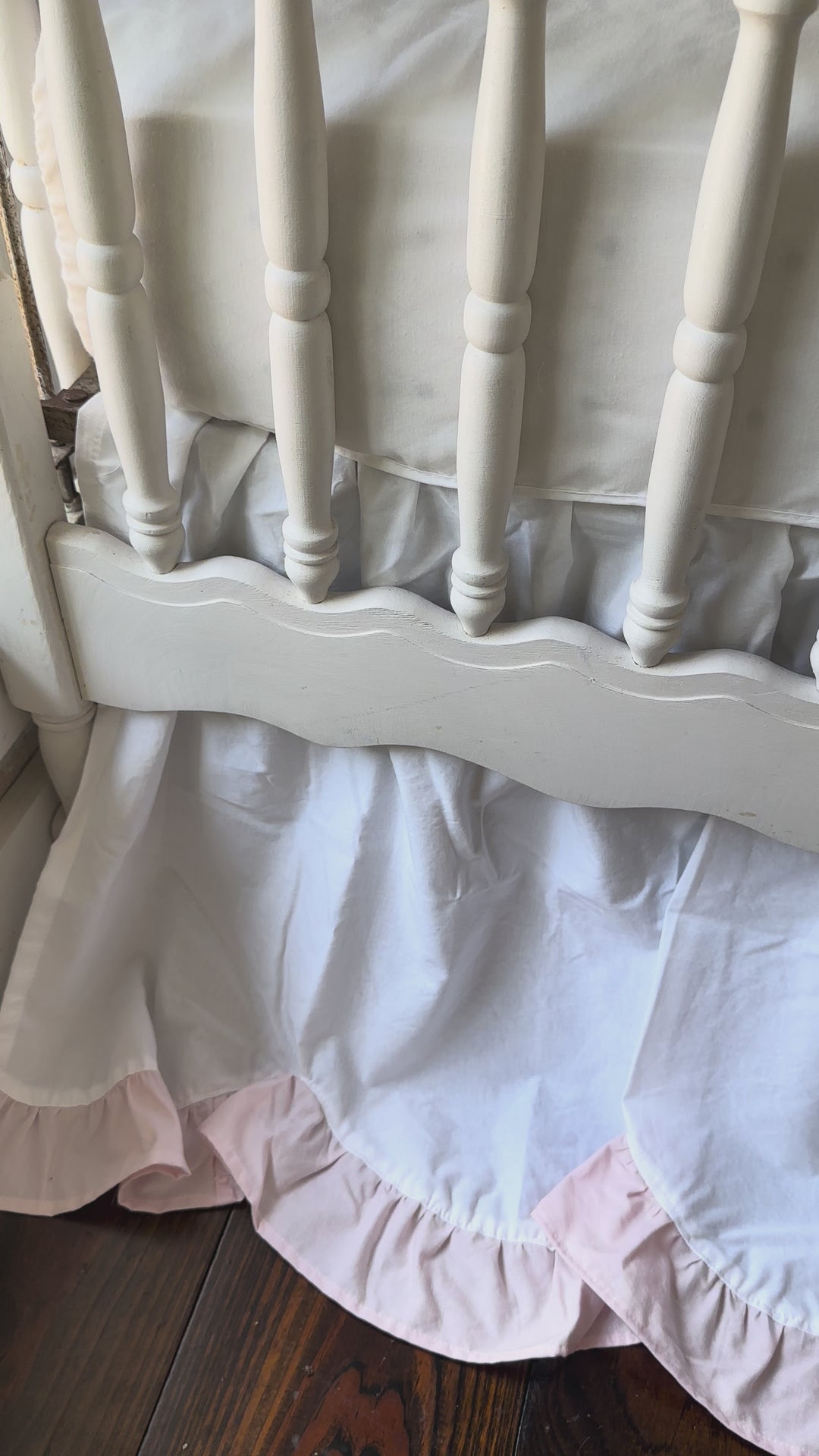 Video of the white and baby pink scalloped crib skirt moving gently on a spindle crib