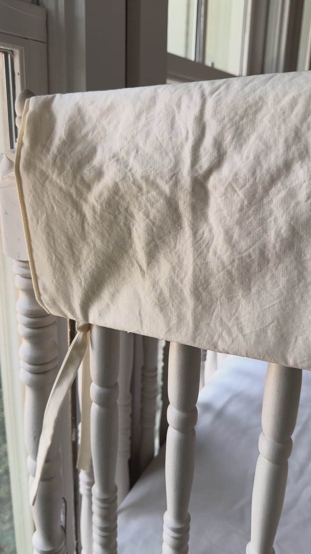 Ivory simple crib rail cover being tied onto the top rail of a white spindle crib.