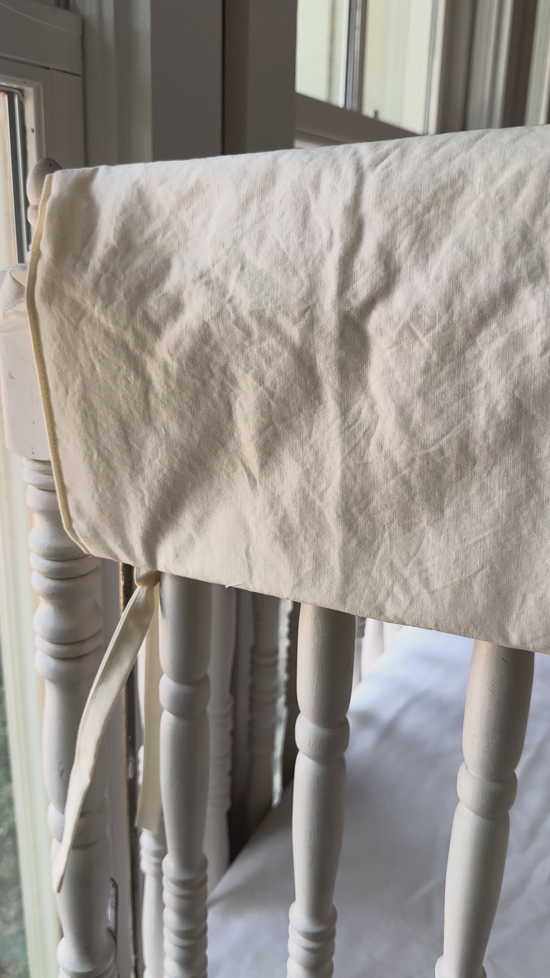 Ivory simple crib rail cover being tied onto the top rail of a white spindle crib.