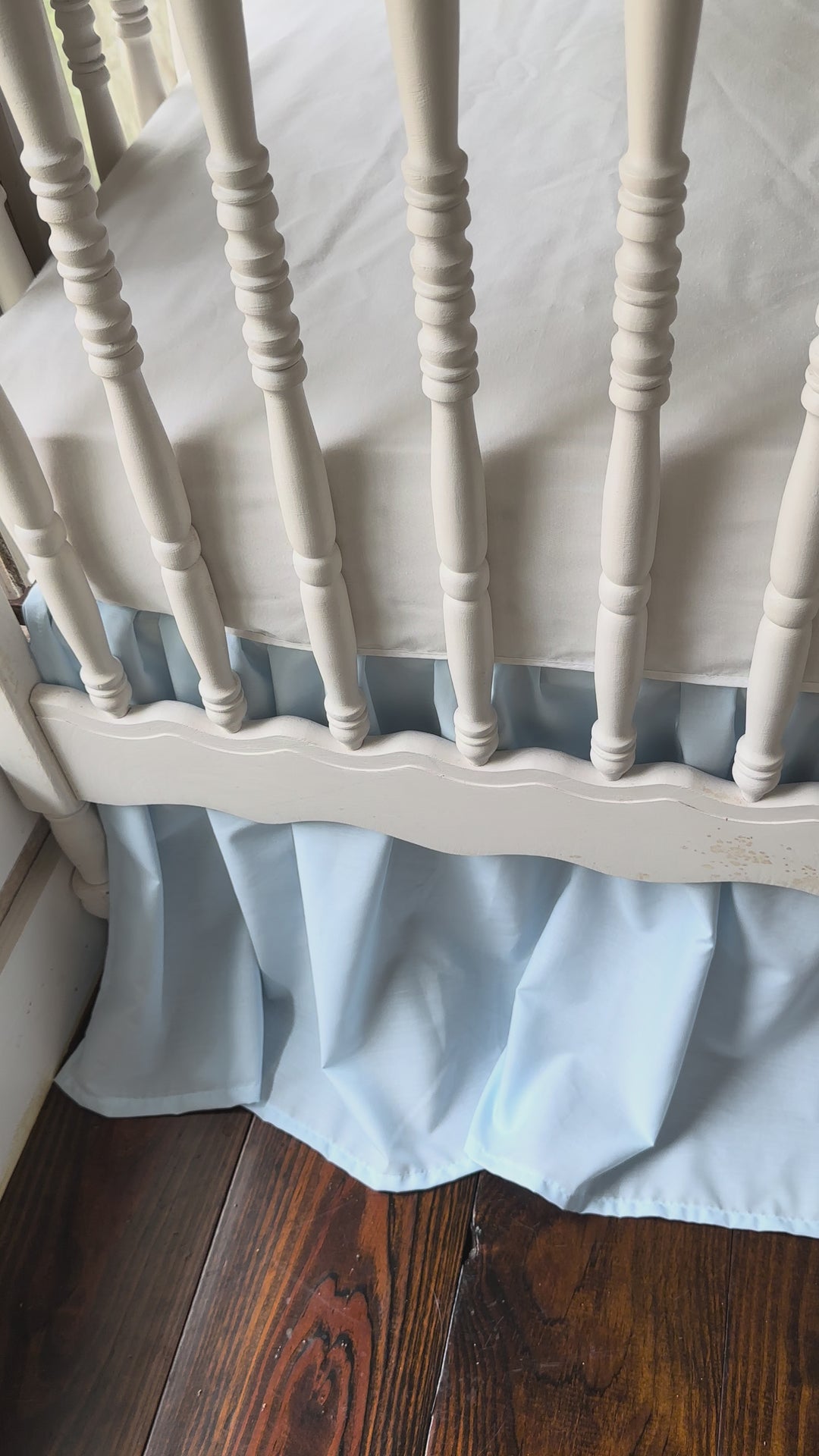 White scalloped crib rail cover with heirloom blue ruffles and matching farmhouse skirt styled on a crib.