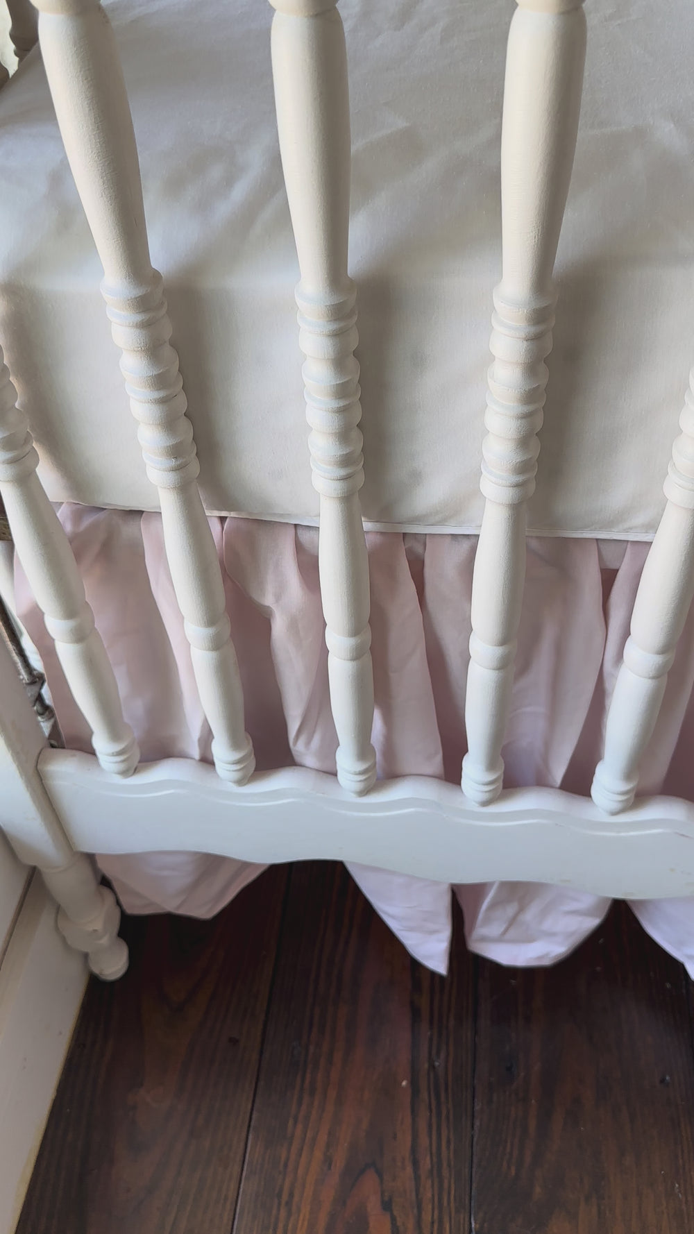 Walking video of the baby pink farmhouse crib skirt and two large pink bows on a white spindle crib