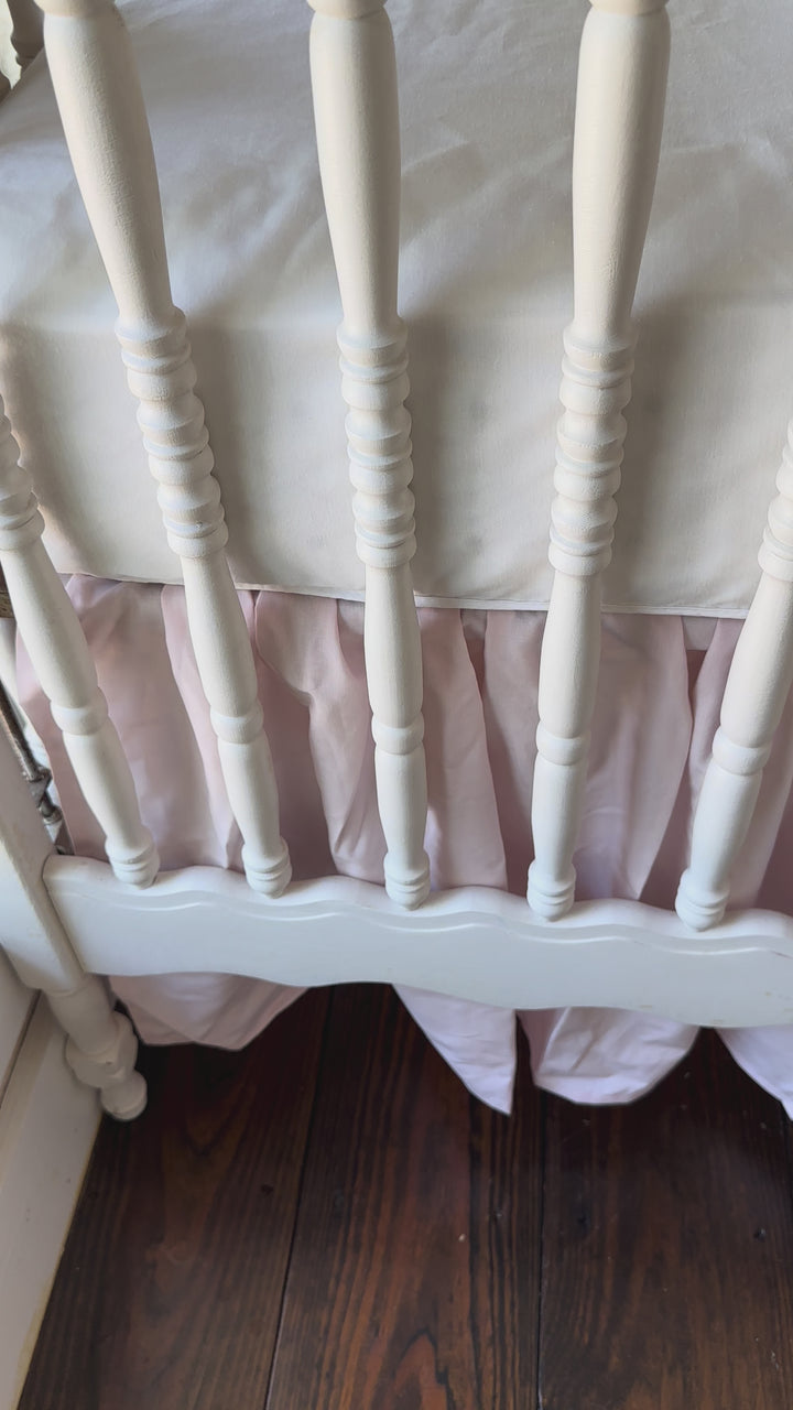 Walking video of the baby pink farmhouse crib skirt and two large pink bows on a white spindle crib