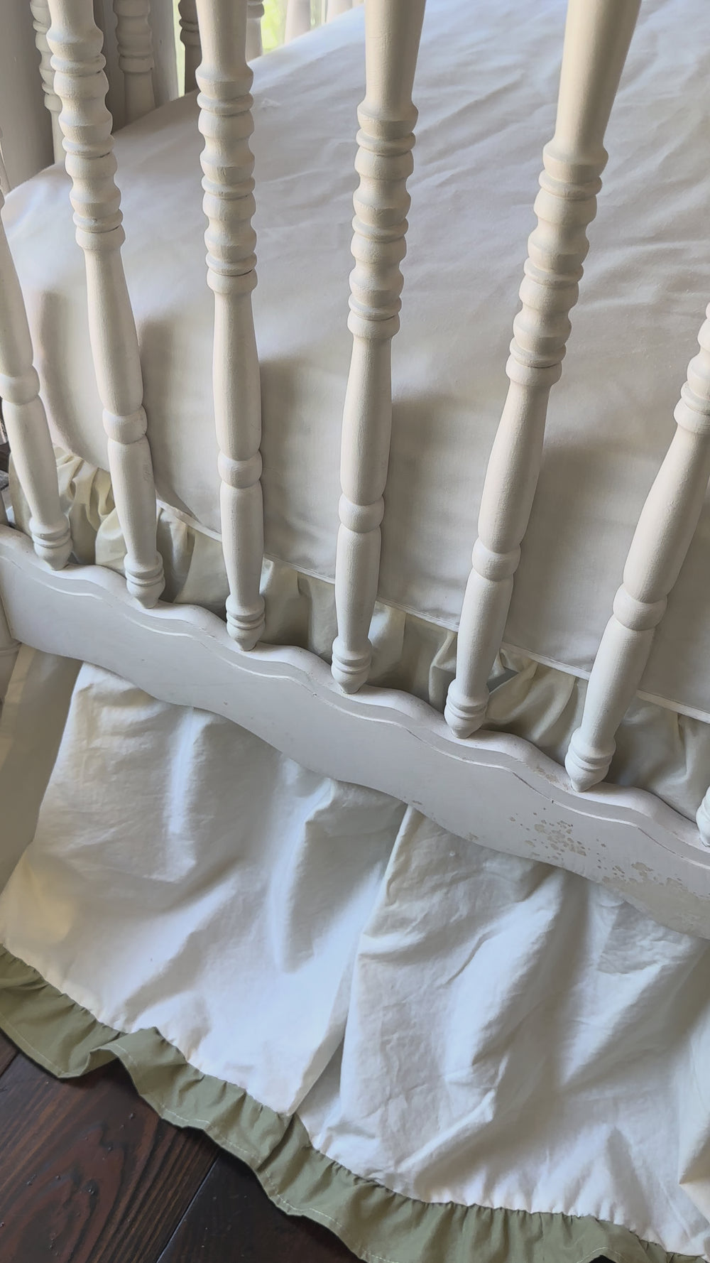 Video of an ivory and sage green ruffled crib skirt showing the gathered 22 inch drop on a white spindle crib