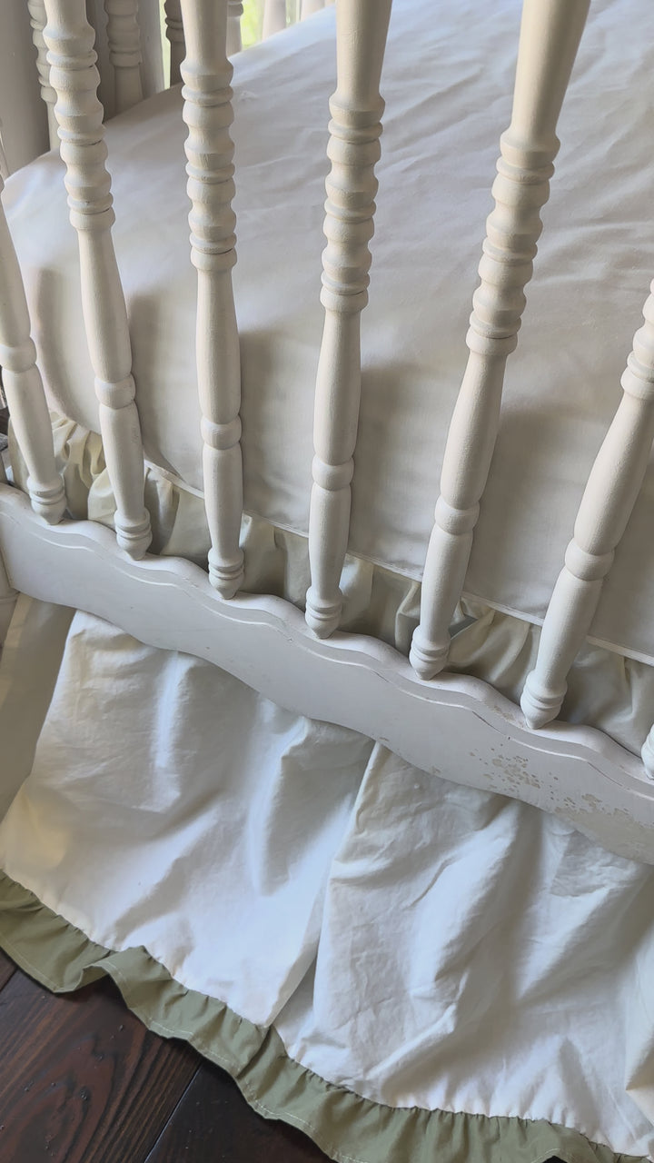 Video of an ivory and sage green ruffled crib skirt showing the gathered 22 inch drop on a white spindle crib
