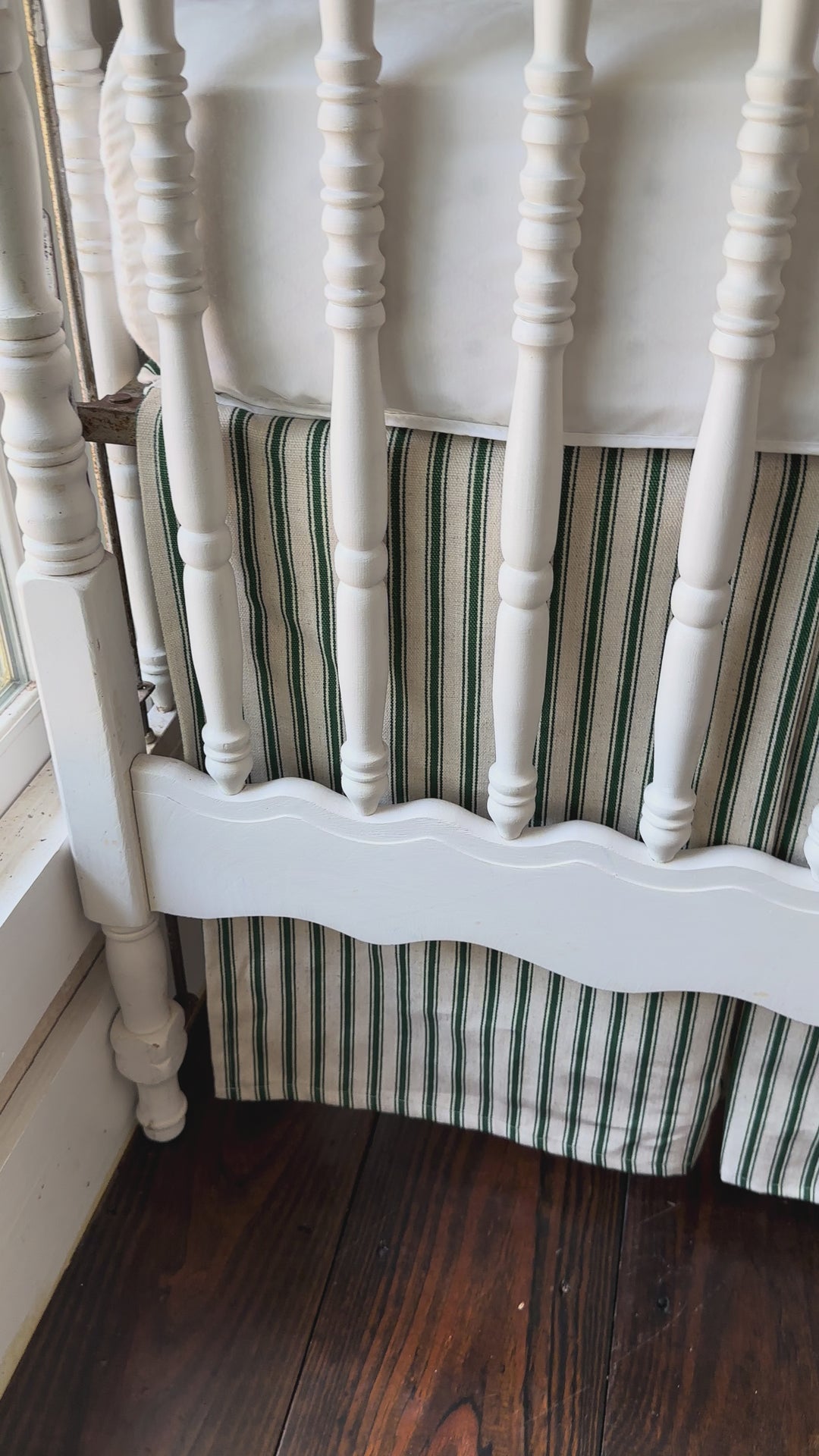Walking video of the pine green ticking tailored crib skirt on a white spindle crib