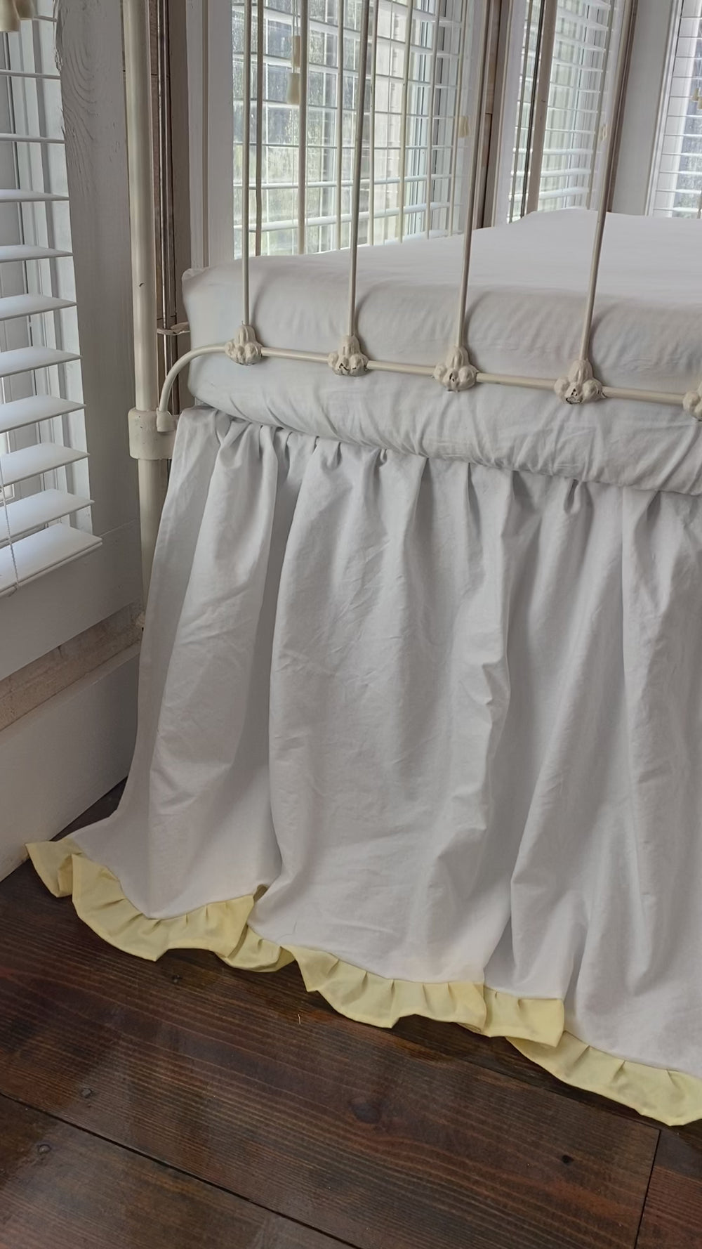 Video of white and baby yellow ruffled crib skirt on iron crib in a baby's nursery