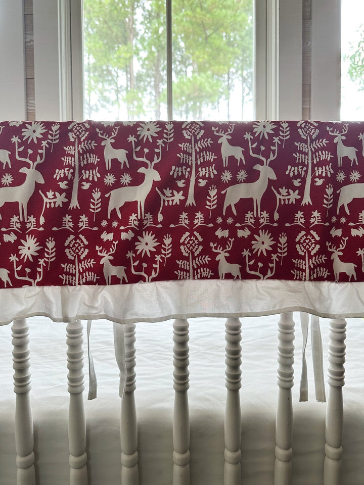 Red and white folk deer ruffled crib rail cover on the long rail of a white spindle crib