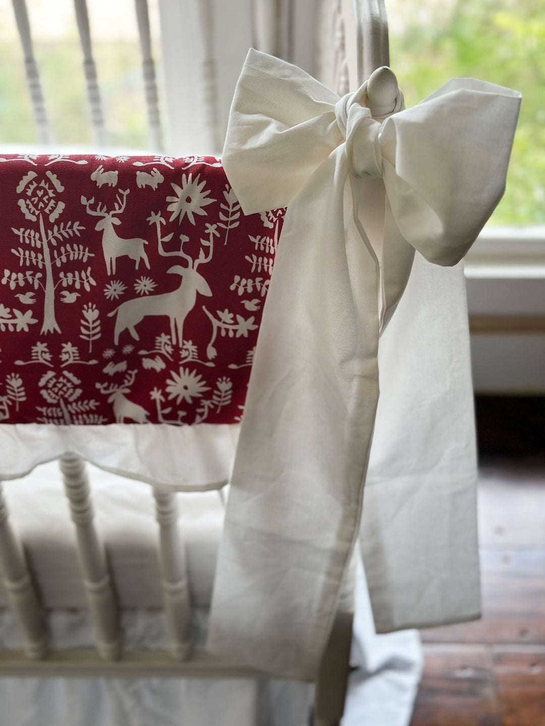 Close view of the folk deer print showing stags, trees and flowers in white on cranberry red