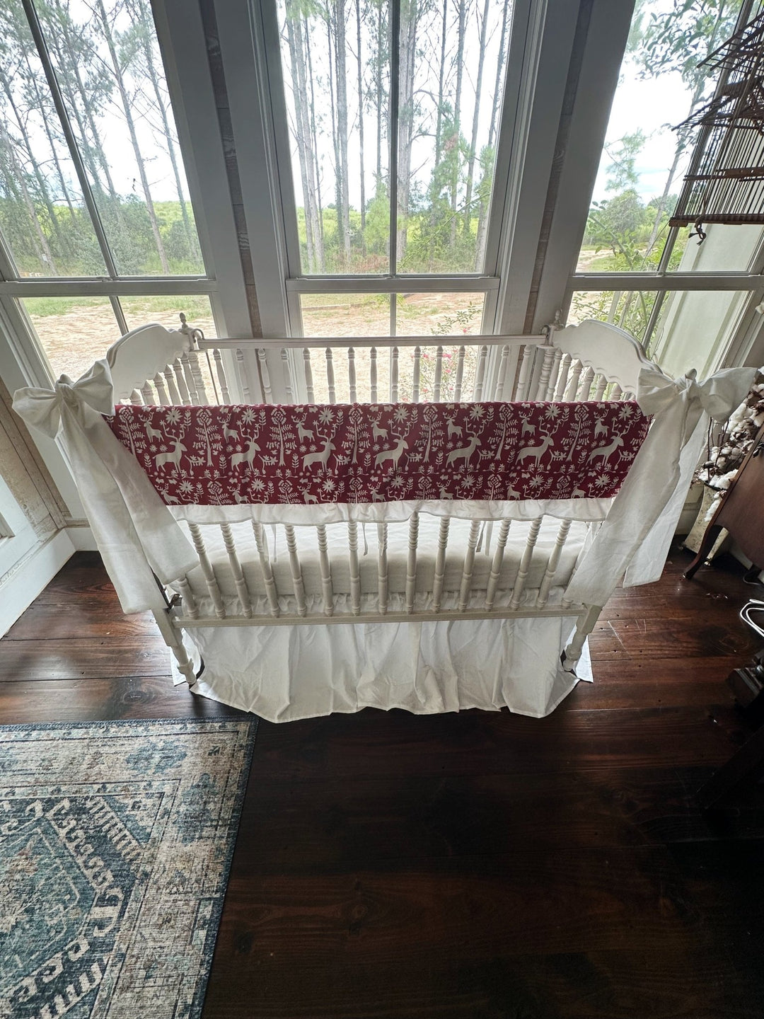 Crib dressed in the red folk deer rail cover, white gathered skirt and white corner bows, seen from above