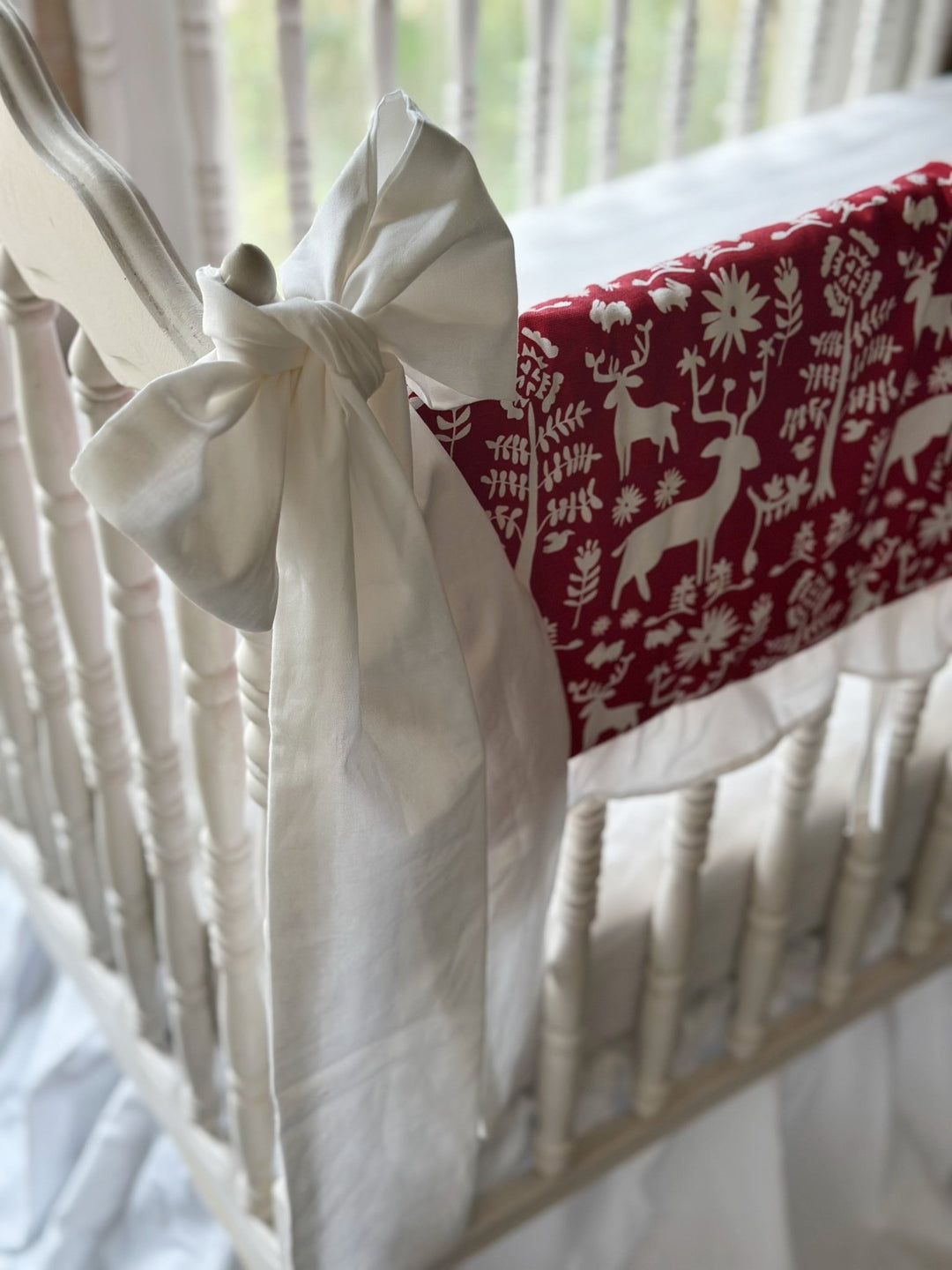 Large white bow tied to the crib post beside the cranberry red deer print rail cover