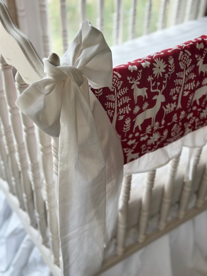 Large white bow tied to the crib post beside the cranberry red deer print rail cover