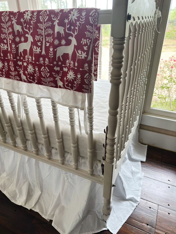 End of the folk deer rail cover where it wraps the crib post, white ruffle and ties below