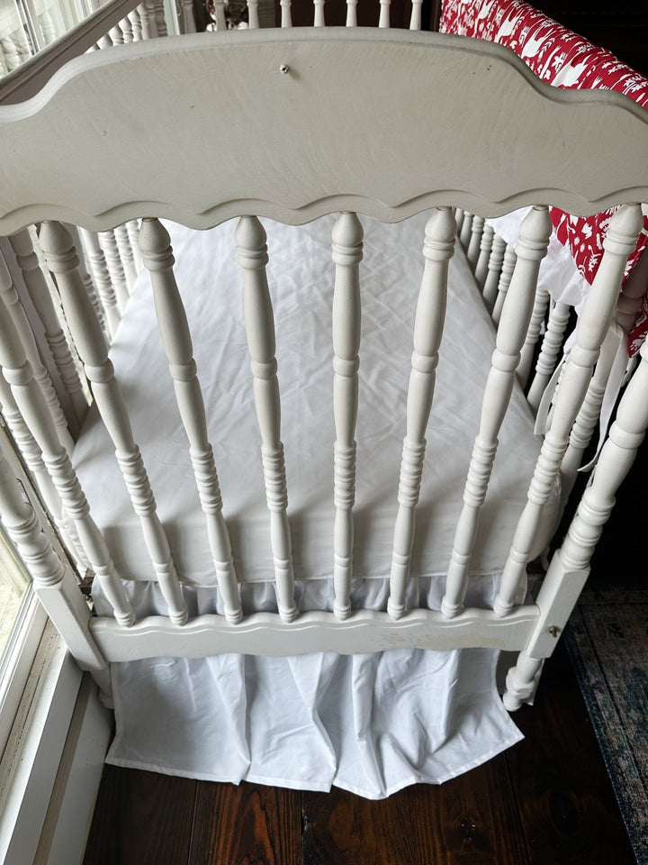 Looking down into the crib at the white fitted sheet with the gathered white skirt below
