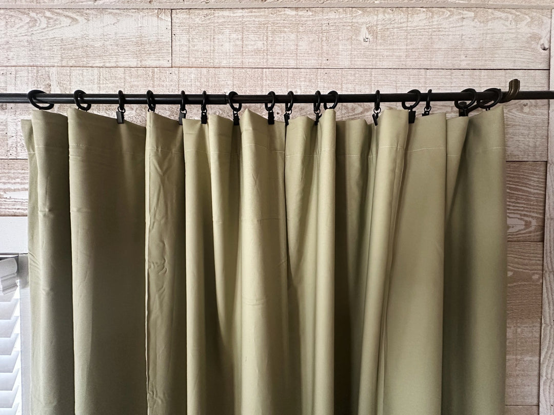 Header of the sage green curtains hung from black clip rings on an iron rod, soft folds falling from each clip