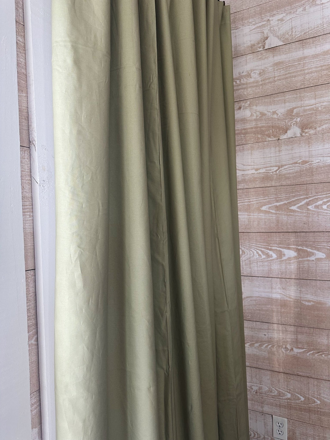 Side view of a sage green blackout panel falling in long even folds next to a whitewashed shiplap wall