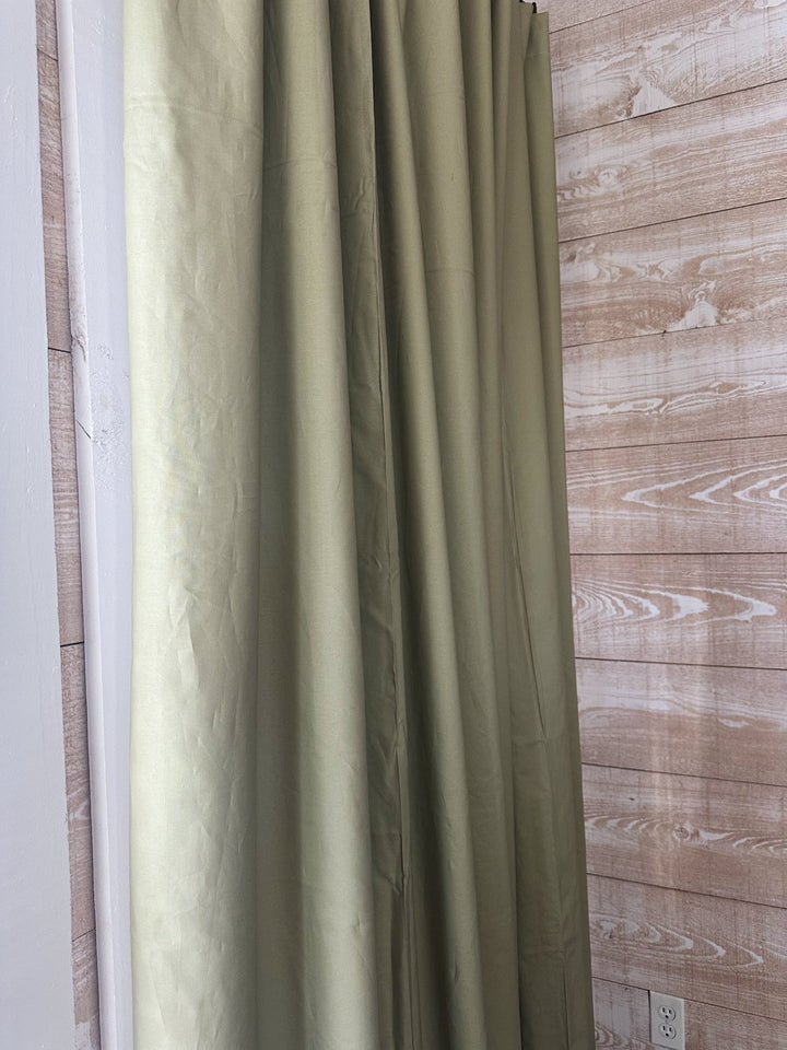 Side view of a sage green blackout panel falling in long even folds next to a whitewashed shiplap wall