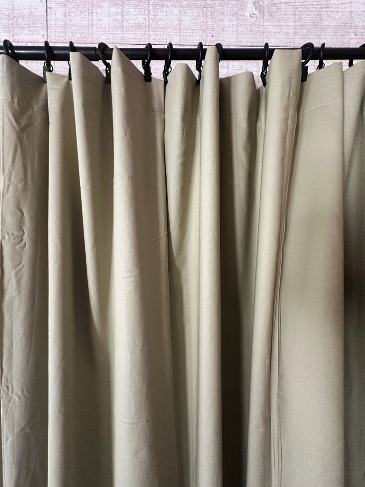 Close view of the sage curtain tops gathered into folds beneath a row of black curtain rings