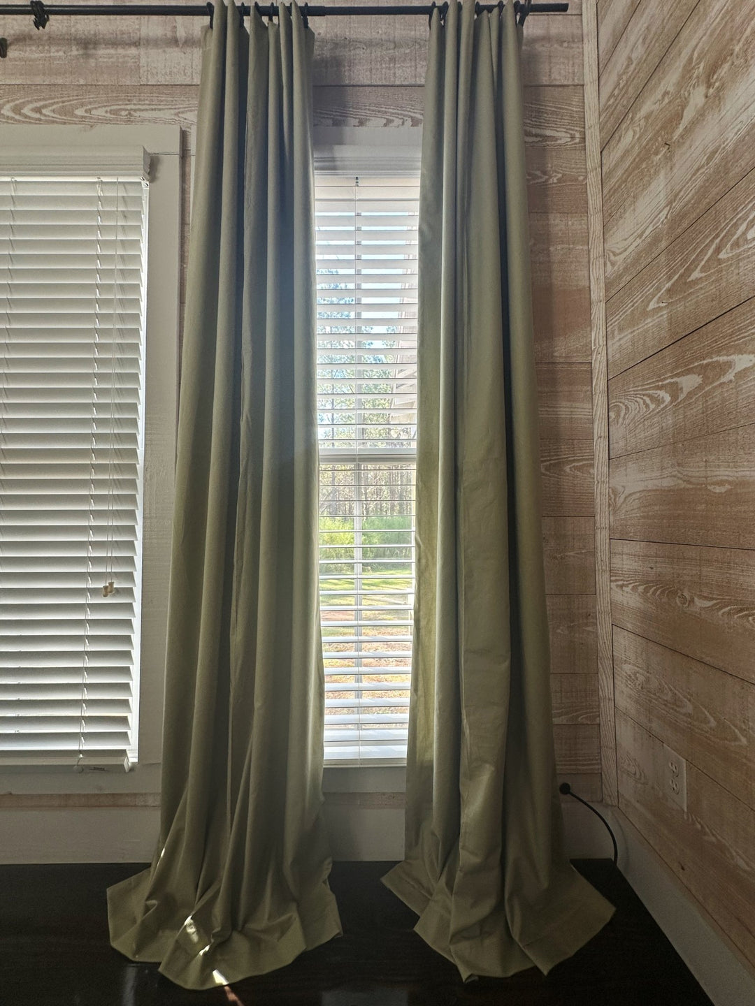 Daylight and pine trees showing through the gap between two sage green blackout panels, the closed fabric holding back the light