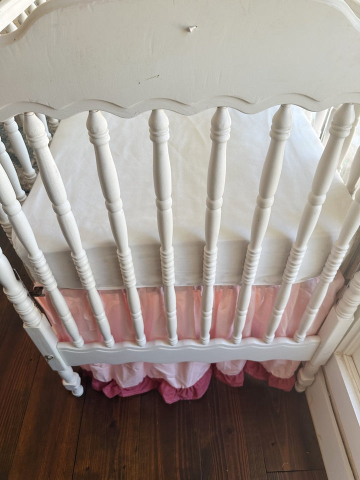 Looking down over the scalloped footboard at the white mattress, with the Sisters Pink skirt and blush ruffle beneath