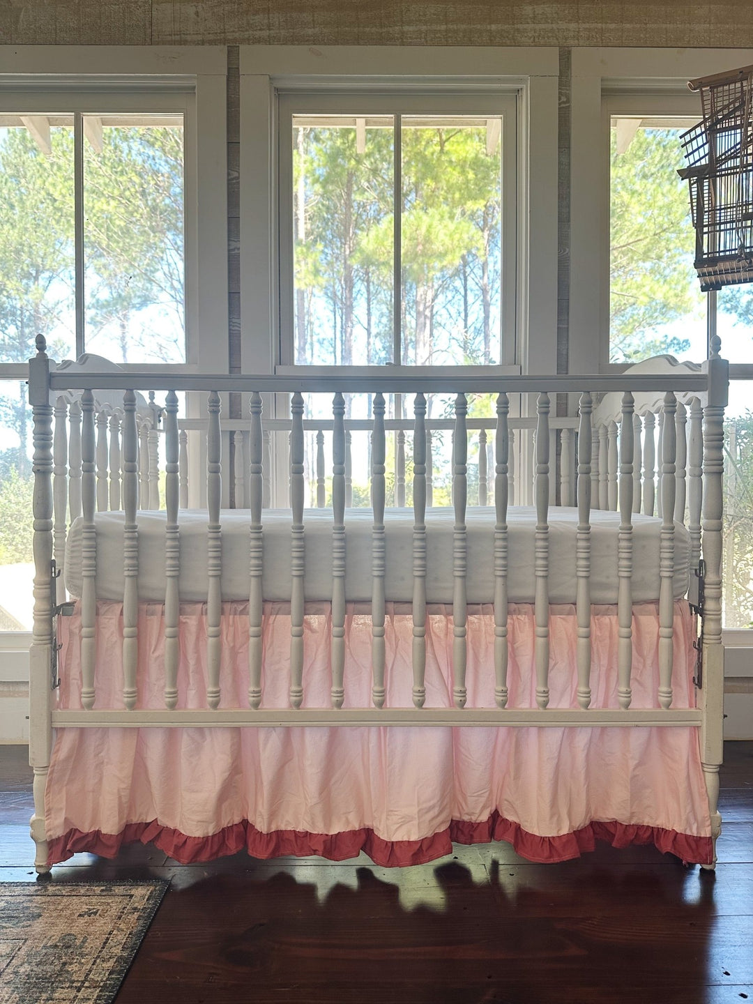Sisters Pink & Blush ruffled cotton crib skirt on a white spindle crib, straight-on front view in front of three tall windows