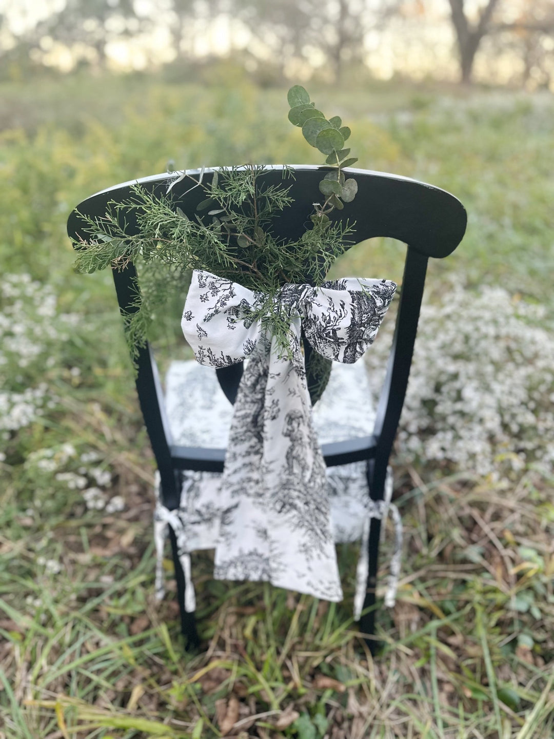 Matching toile bow tied over cedar and eucalyptus on a dressed dining chair