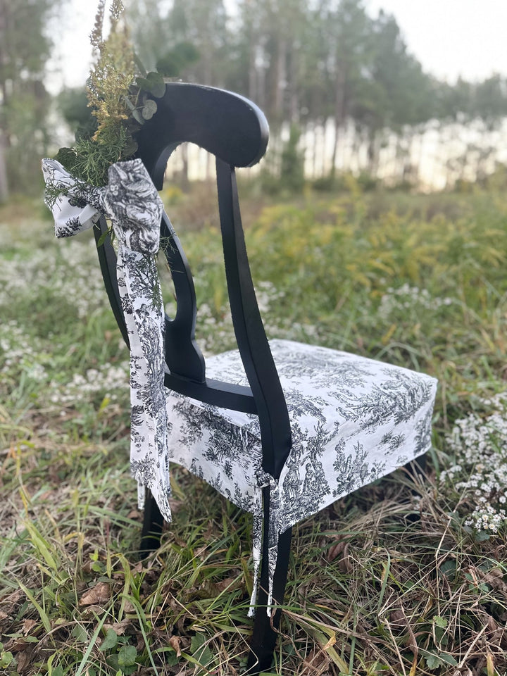 Side angle of the chair with a long toile bow hanging from the back and the seat slipcover below
