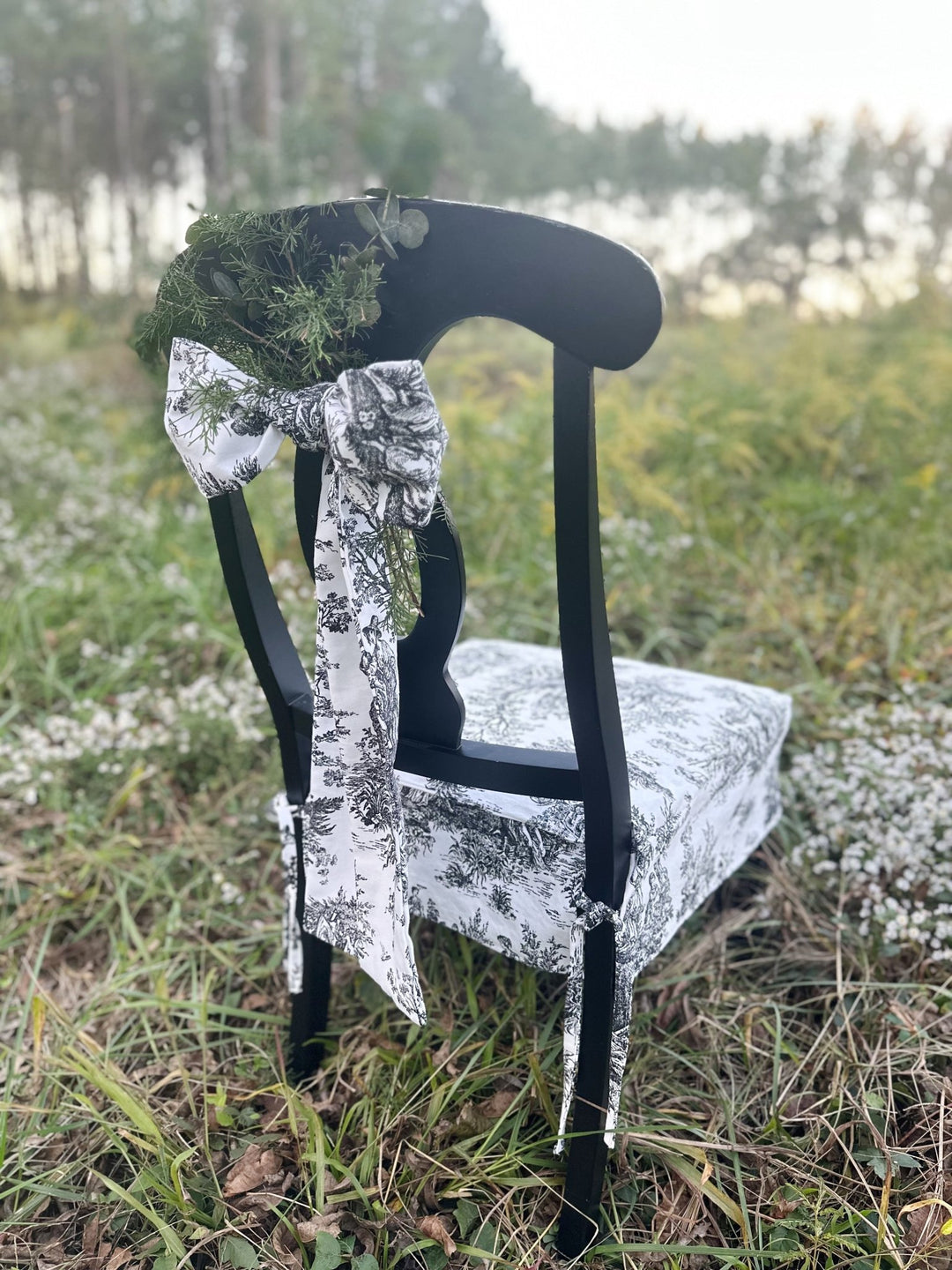 Toile bow and greenery on the back of a dining chair dressed for a holiday table