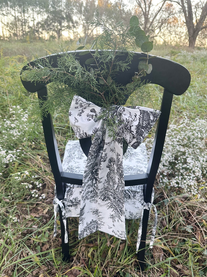 Toile chair back bow with long tails and fresh greenery, styled for holiday entertaining