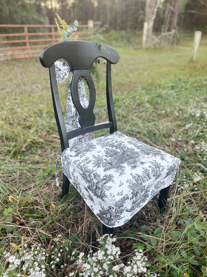 Angled front view of a black and white toile seat cover fitted snugly over a dining chair seat