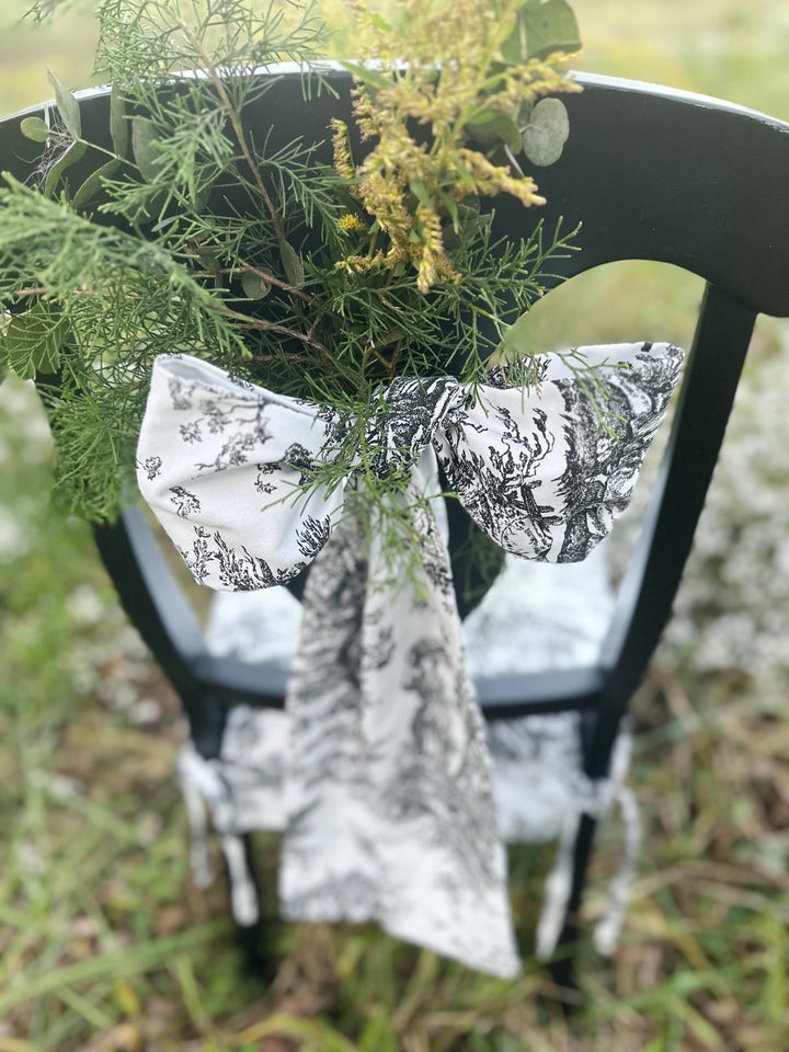 Close-up of a toile sash bow with goldenrod and cedar on a black chair back