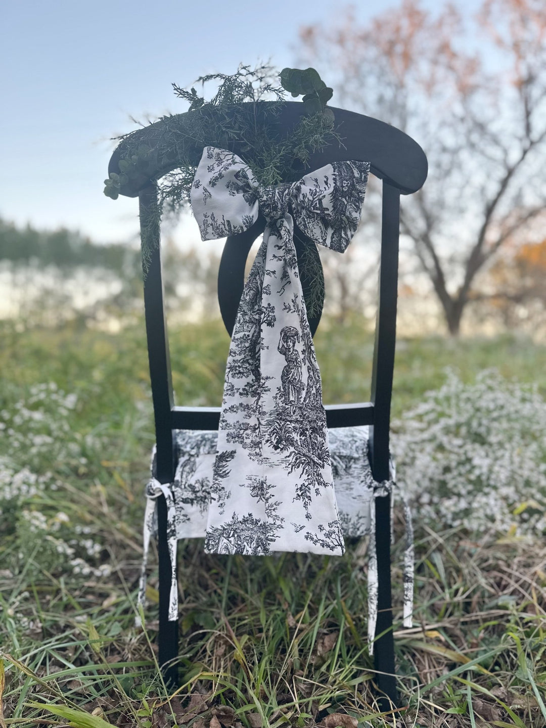 Back of a black chair with a black and white toile sash bow and tailored seat cover, set outdoors